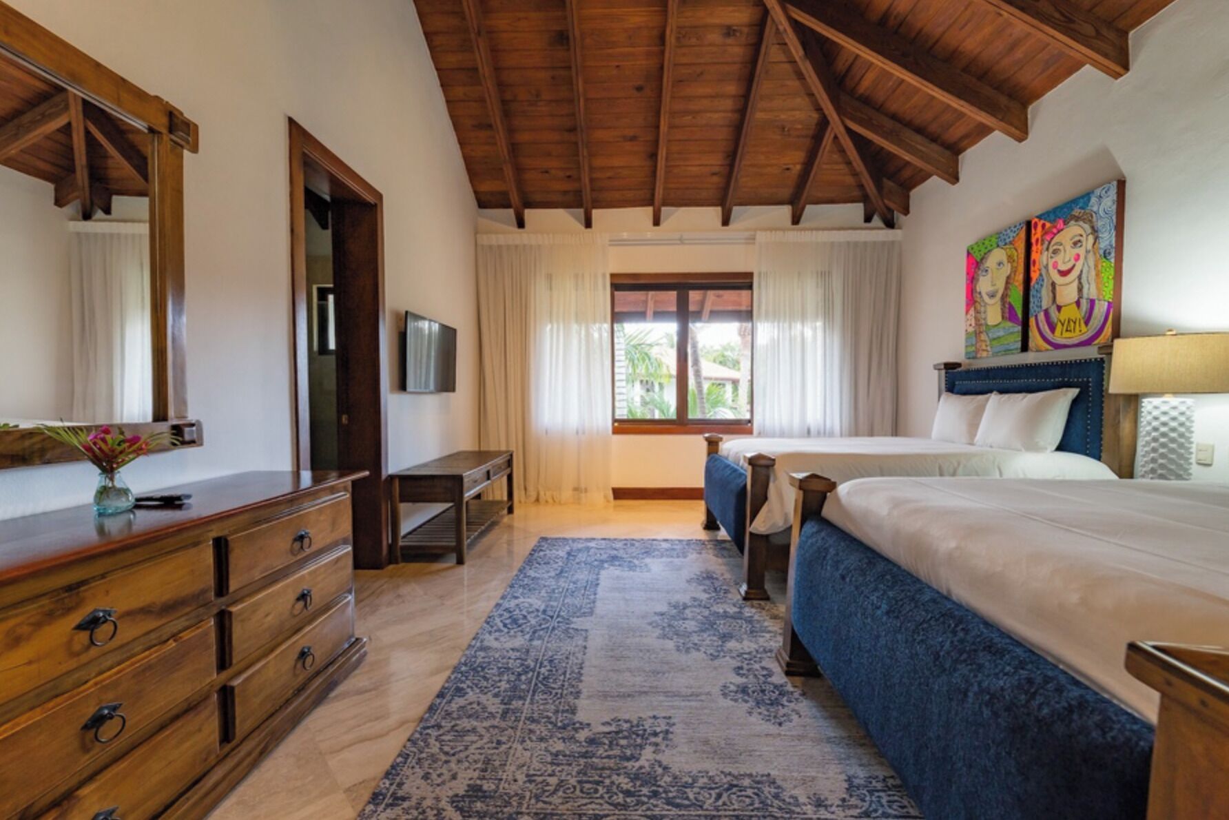 Une chambre à coucher avec un plafond en bois, un lit, une commode, un téléviseur et une fenêtre avec des rideaux.
