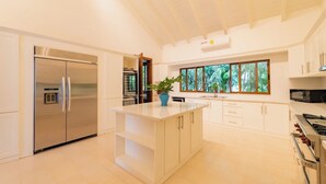 A modern kitchen with a central island, stainless steel appliances, and large windows providing natural light.