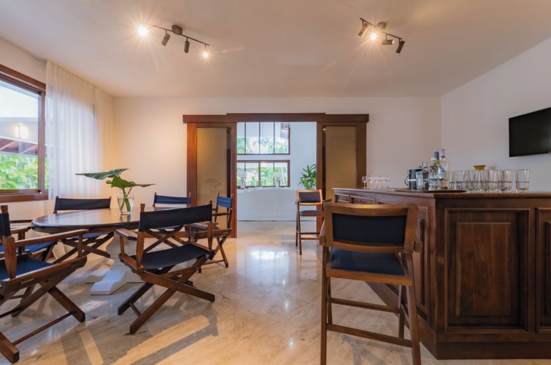 A spacious room with a wooden dining table and chairs, a bar area with glasses and bottles, and a large window providing natural light.