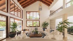 A spacious living room with a high ceiling, large windows, and a view of the outdoors.