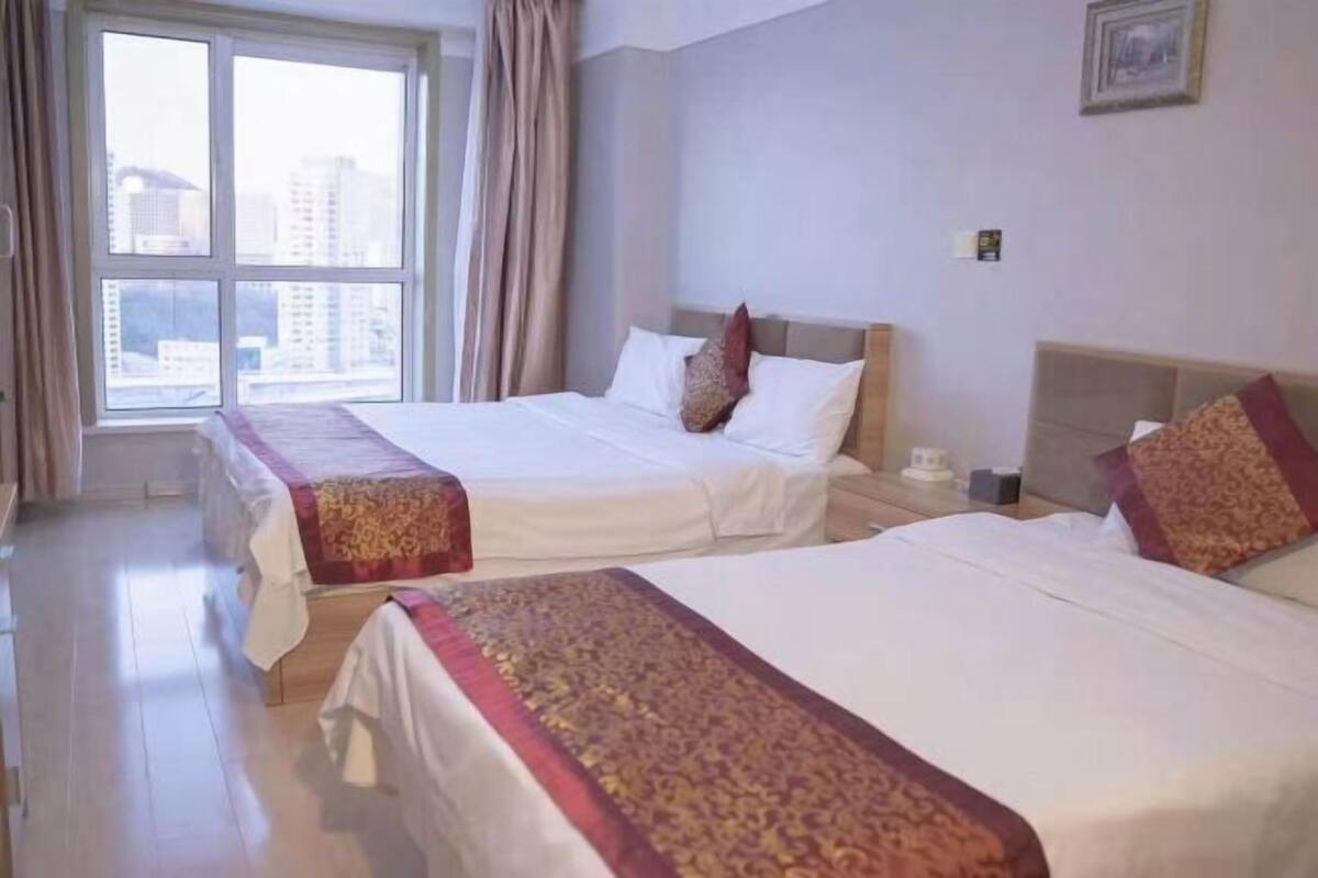 Habitación de hotel con dos camas, un ventanal grande y vistas a la ciudad.