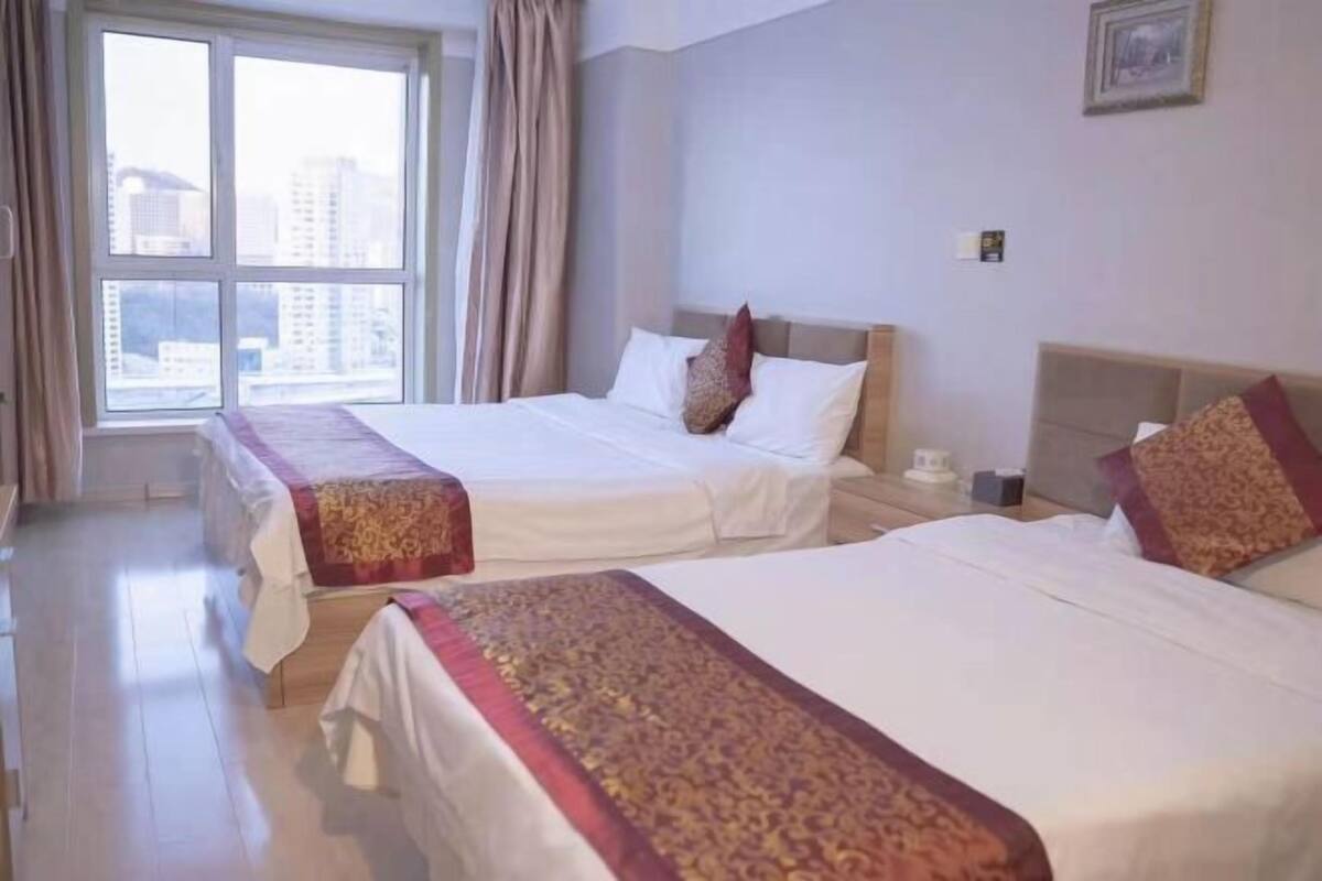 Habitación de hotel con dos camas, un ventanal con cortinas, un cuadro en la pared y una mesita de noche con lámpara.