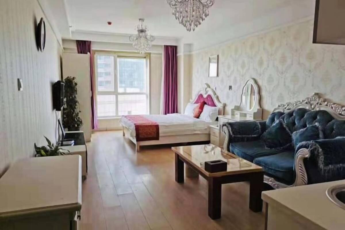 Un dormitorio con cama, tocador, sofá azul, candelabro y un ventanal grande.