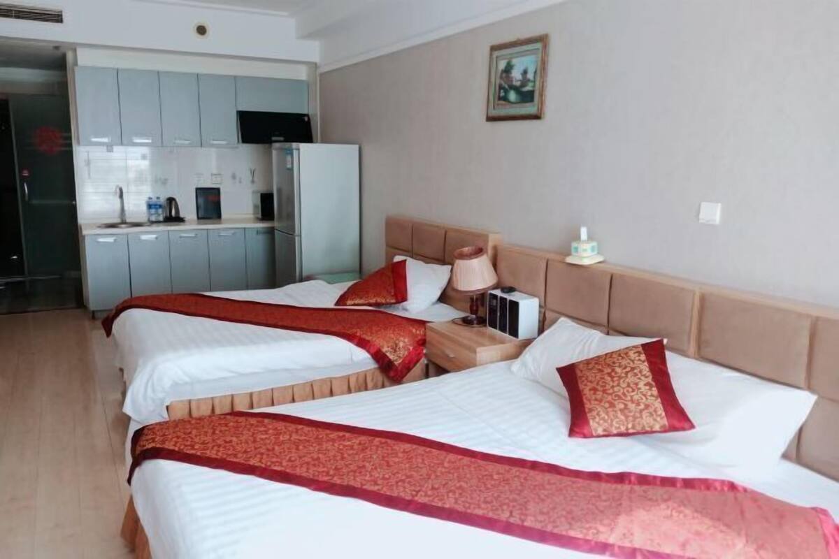 Una habitación de hotel con tres camas, un kitchenette y un cuadro en la pared.