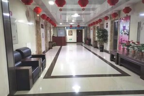 A hotel reception area with a reception desk, seating area, and potted plants.