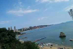 Vista costera con una gran extensión de agua, un promontorio rocoso y un horizonte urbano distante.