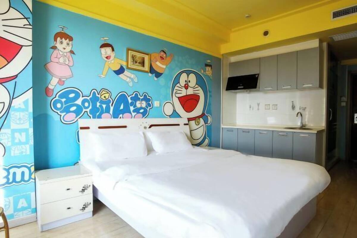 Un dormitorio con cama, mesita de noche, pared decorada con personajes de dibujos animados y kitchenette.