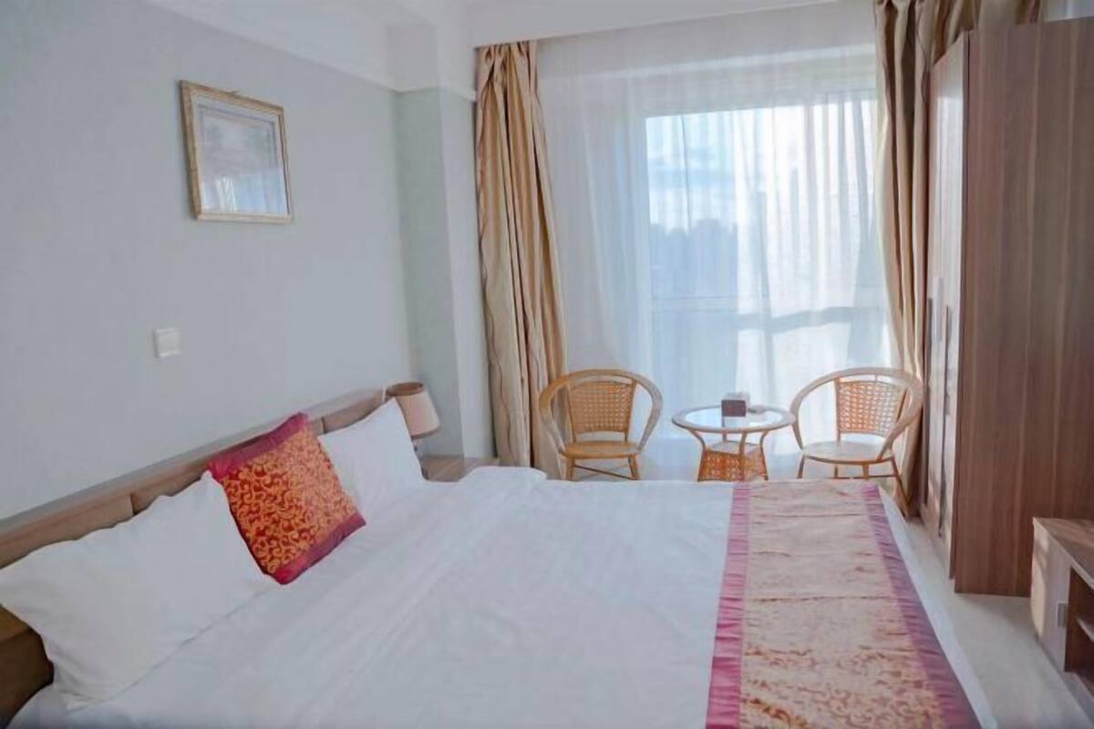 Una habitación de hotel con cama, dos sillas, una mesita y una ventana con cortinas.