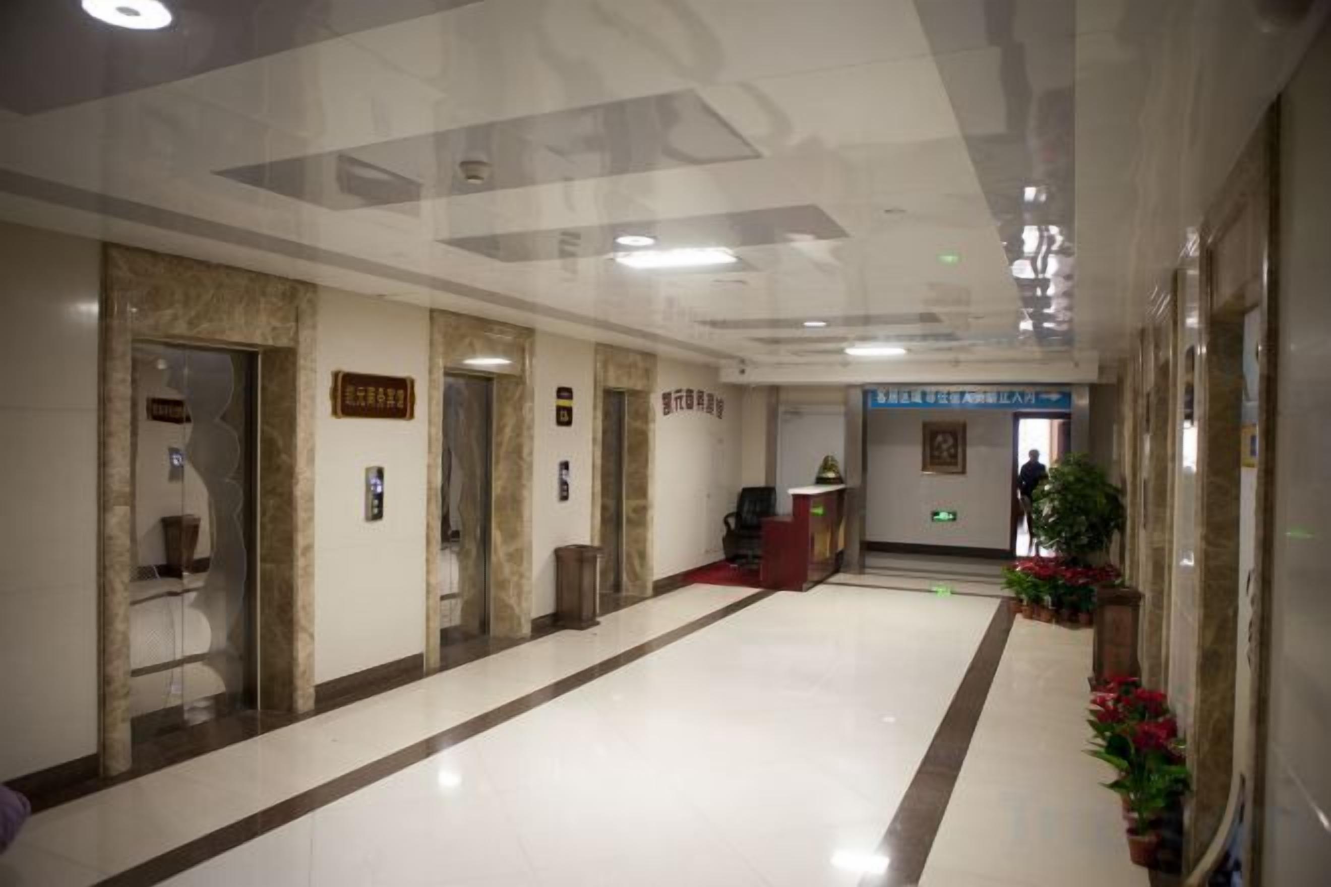A hallway with elevators, a reception desk, and potted plants.