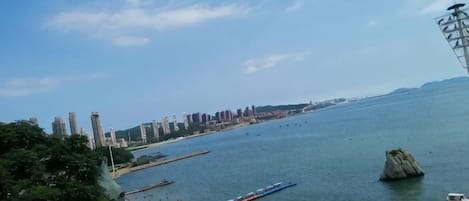 A coastal cityscape with a large body of water, a prominent rock formation, and a distant skyline of buildings.