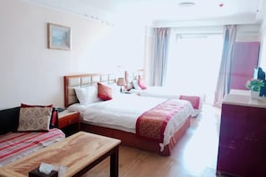 Une chambre d’hôtel avec deux lits, une table en bois, un bureau et une fenêtre avec des rideaux.