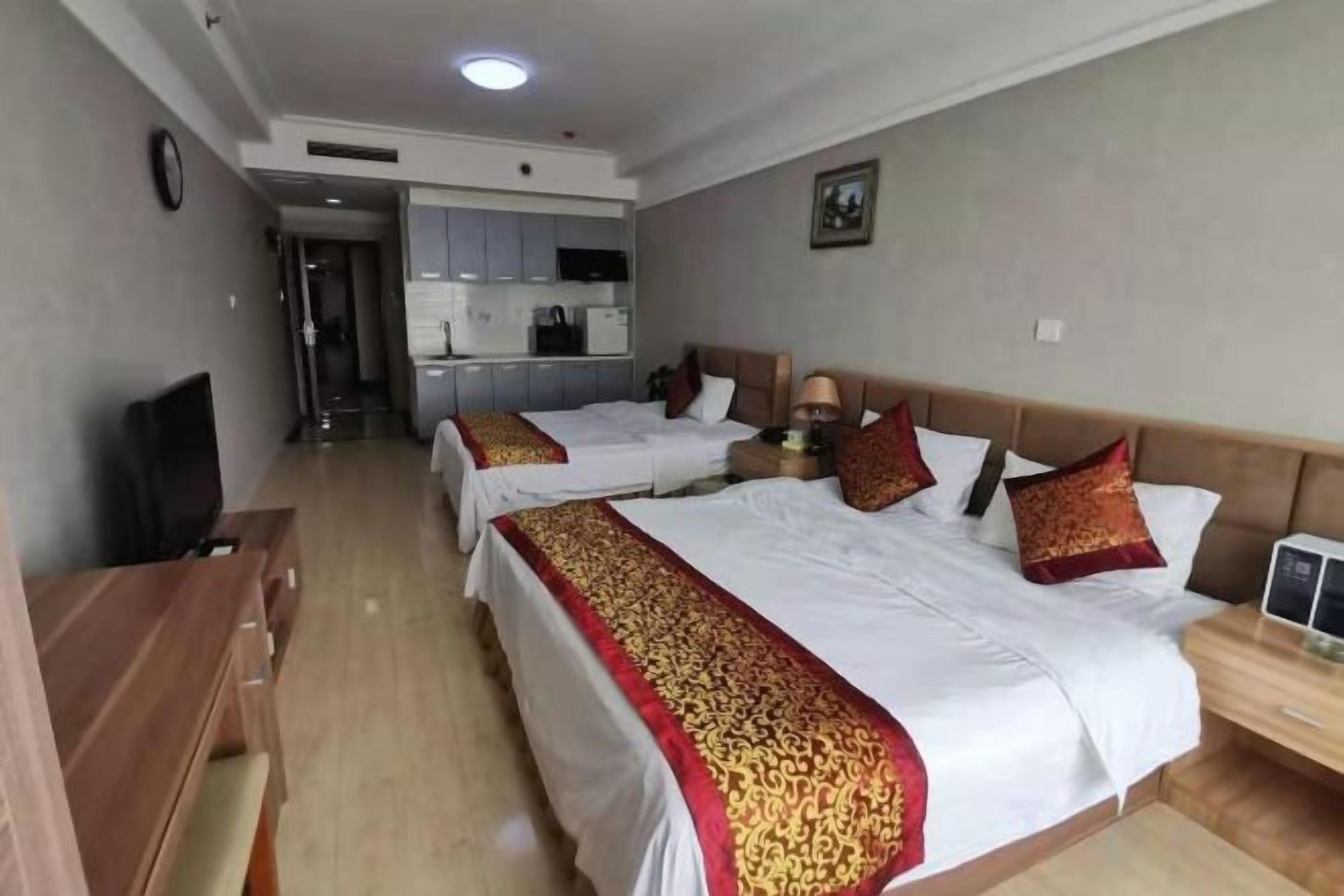 A hotel room with two beds, a desk, a TV, and a kitchenette.