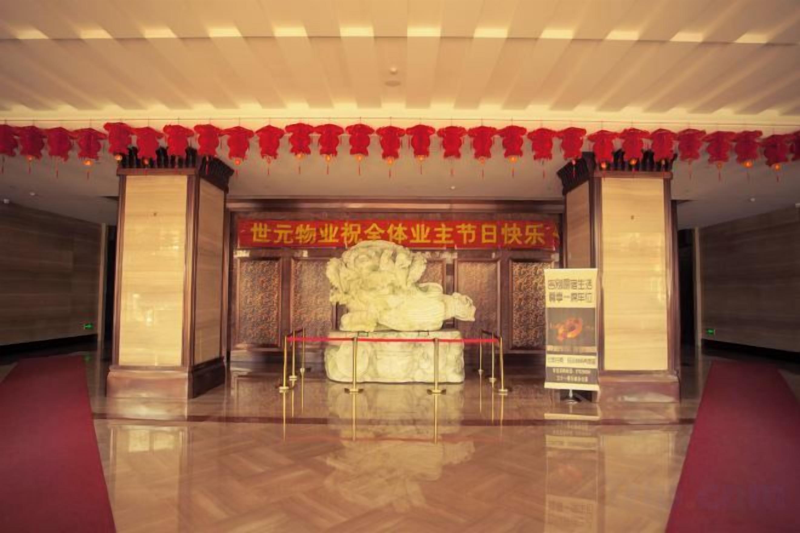 Una zona de recepción con alfombra roja, una estatua grande y un cartel.