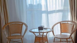 Kaksi rottinkituolia ja pieni pyöreä pöytä, jonka päällä on radio, on sijoitettu ikkunan lähelle, jossa on läpikuultavat verhot.