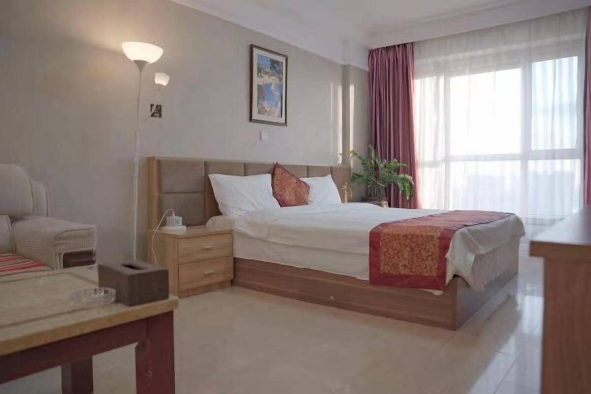 Una habitación de hotel con cama, mesita de noche, lámpara y ventana con cortinas.