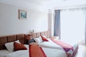 Une chambre d’hôtel avec deux lits, un tableau au mur et une fenêtre avec des rideaux.