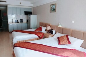 Une chambre d’hôtel avec trois lits, une kitchenette et un tableau au mur.