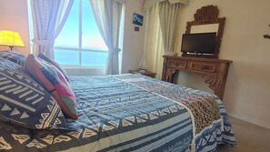 A bedroom with a bed, curtains, a television, and a wooden dresser. - Oceana Suites Bahía Pelicanos (Puchuncavi)