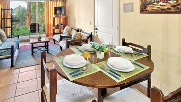 Zona pranzo con tavolo apparecchiato per quattro persone, un divano e una televisione sullo sfondo.
