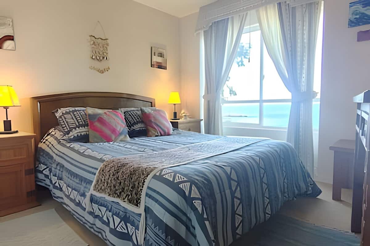 Une chambre à coucher avec un lit, deux lampes de chevet, une fenêtre avec des rideaux et une vue sur la mer.