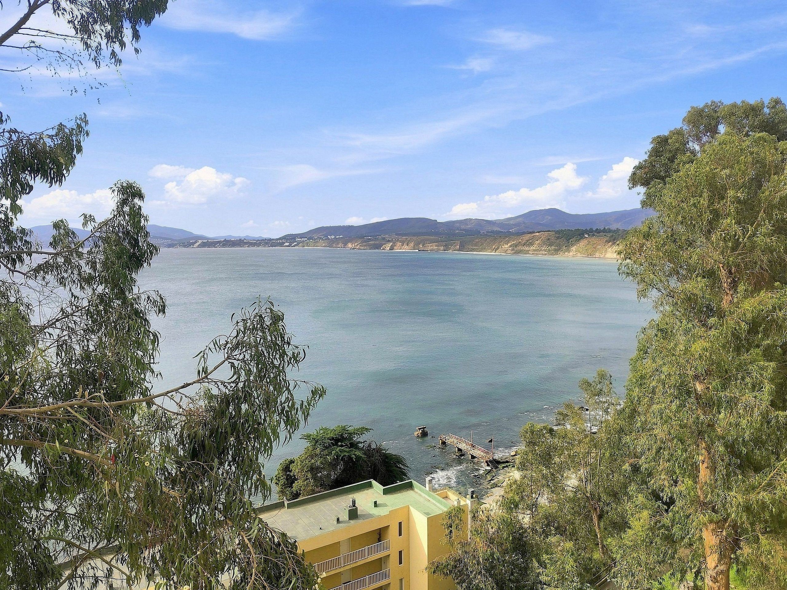 A coastal view with a building in the foreground and a bridge over water.