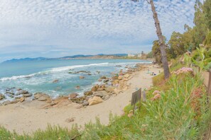 Una playa con costa rocosa, vegetación y montañas a lo lejos.