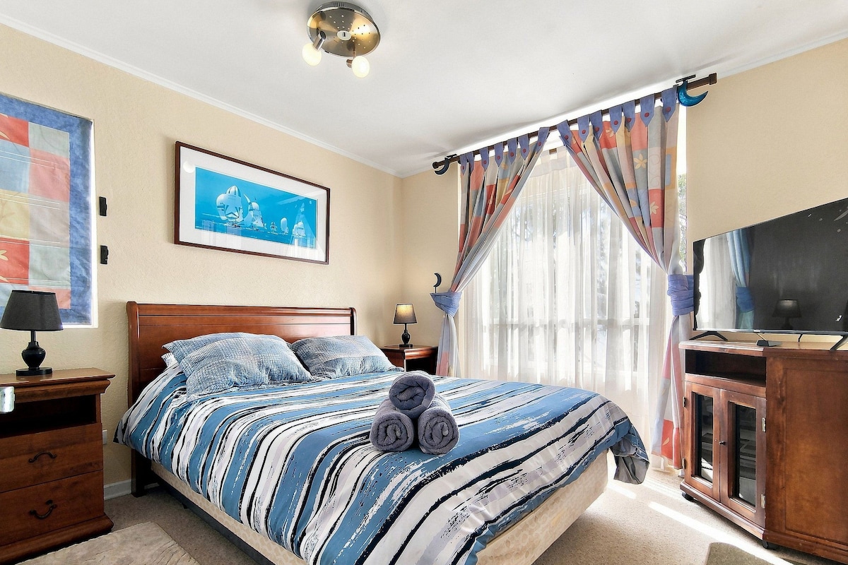 Une chambre à coucher avec un lit, une table de chevet, une lampe, un téléviseur et une fenêtre avec des rideaux.