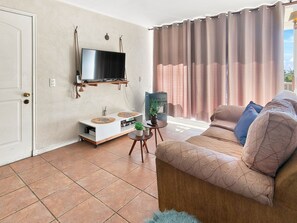 A living room with a sofa, a TV mounted on the wall, a small table with a plant, and a window with curtains. - Oceana Suites Bahía Pelicanos (Puchuncavi)