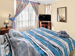 Une chambre d’hôtel équipée d’un lit, d’une télévision, d’un miroir et d’une table de chevet avec une lampe.