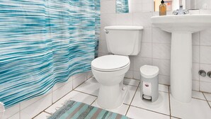 Een badkamer met een douchegordijn met strepen, een toilet, een hygiëneschuimer en een wastafel.