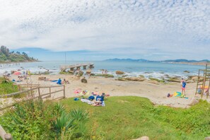 Une plage avec une jetée en bois, des gens qui prennent un bain de soleil et une côte rocheuse.
