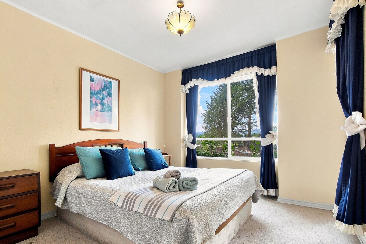 A bedroom with a bed, a nightstand, a window with curtains, and a painting on the wall.