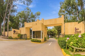 Entrada de un hotel con fachada amarilla, un letrero que dice 'Bahia Pelicanos' y un camino de entrada pavimentado.