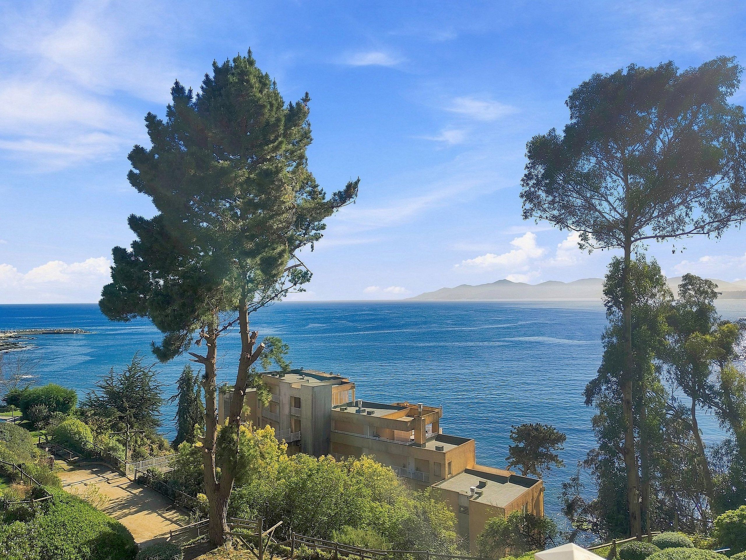 Une vue sur la côte, avec un bâtiment, des arbres et un ciel dégagé.
