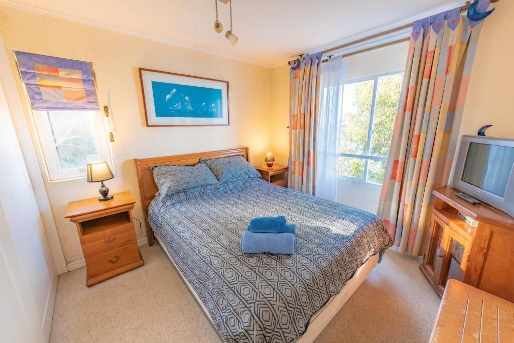 Een slaapkamer met een bed, nachtkastje met lamp, televisie en raam met gordijnen.