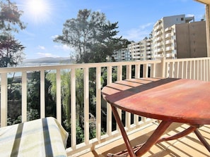 A balcony with a wooden table and chairs, overlooking a residential area with trees and buildings.