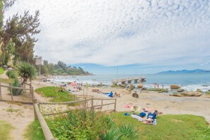 A beach with a wooden pier, people sunbathing, and a rocky shoreline.