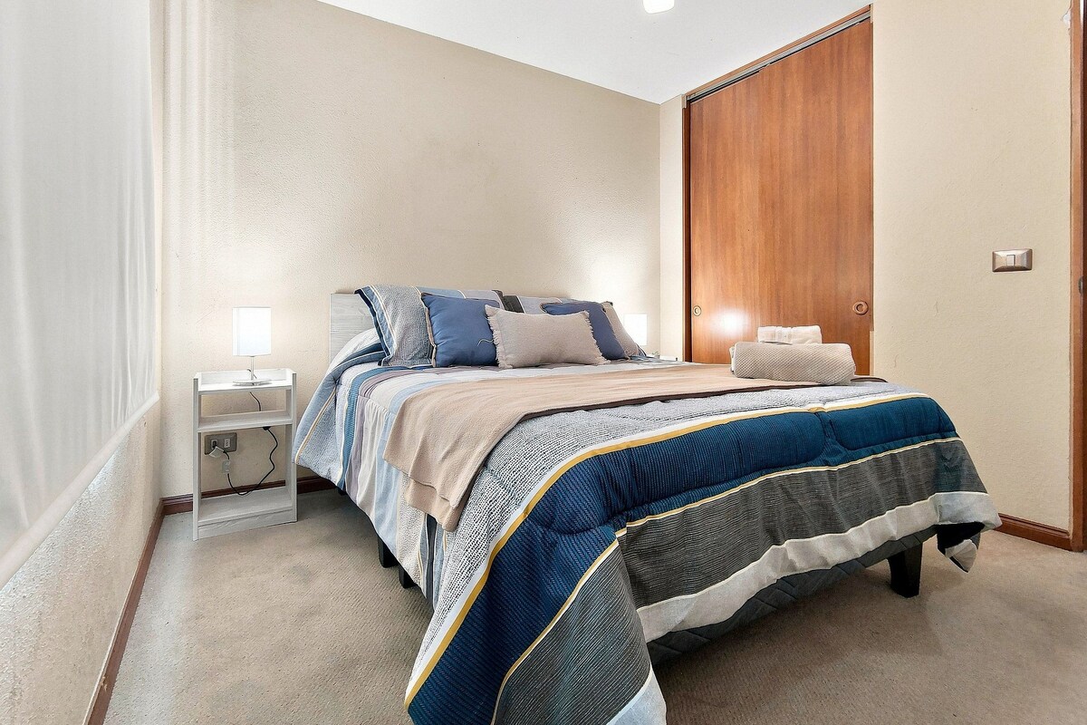 A bedroom with a bed, bedside tables, a nightstand, a wooden wardrobe, and a light fixture.