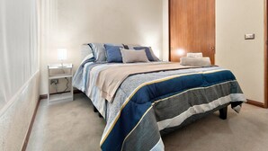 Un dormitorio con cama, mesitas de noche, armario de madera y una lámpara.