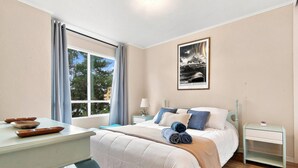 Un dormitorio con cama, mesitas de noche, una ventana con cortinas y un cuadro en la pared.