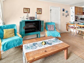 A living room with a television, two chairs, a coffee table, and a door leading to a kitchen. - Oceana Suites Bahía Pelicanos (Puchuncavi)