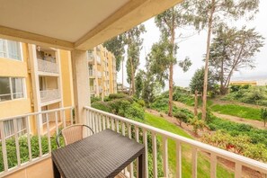Een balkon met een tafel en stoel, met uitzicht op een tuin met bomen en een gebouw op de achtergrond.