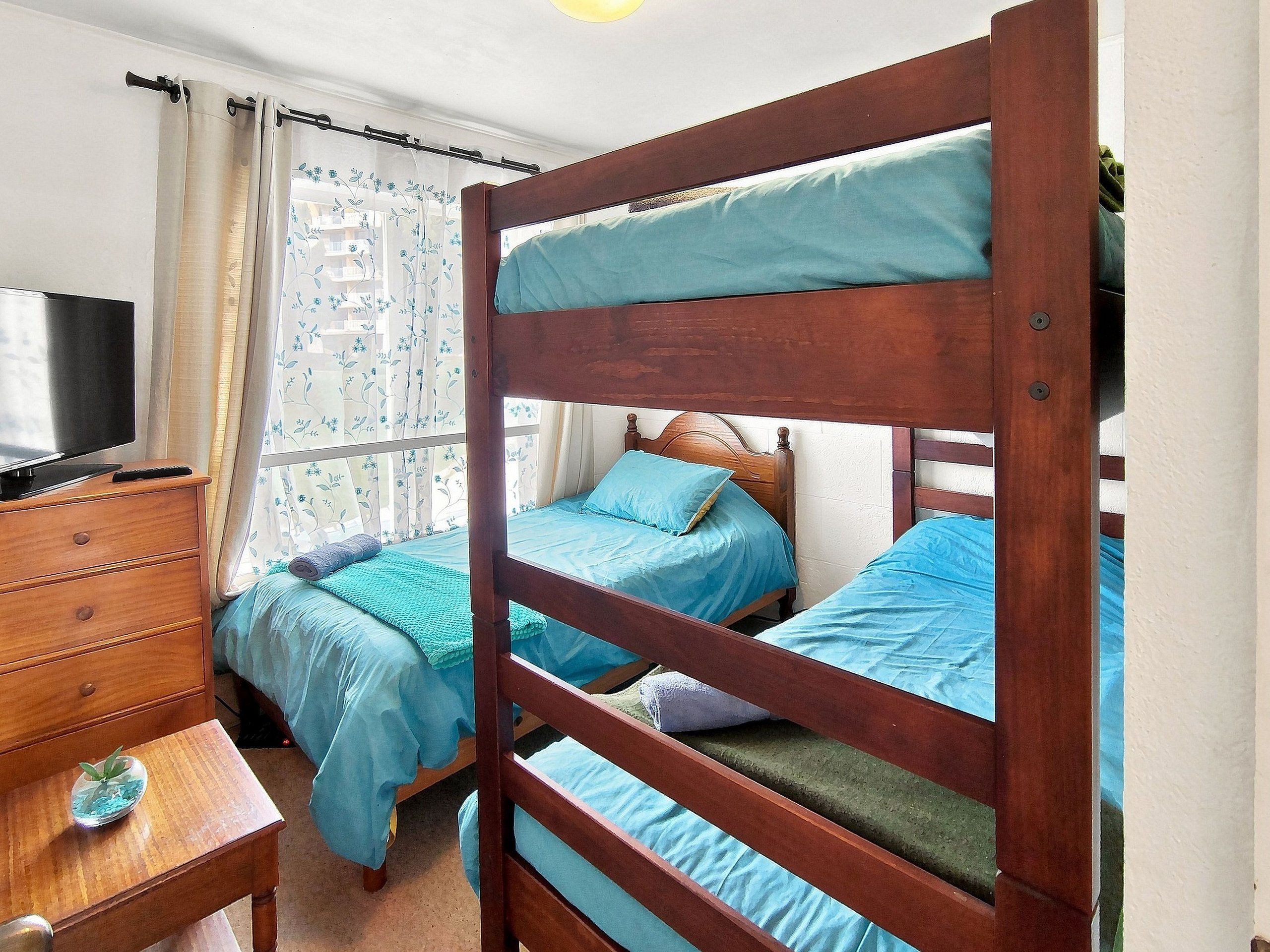 Un dormitorio con dos literas, un aparador de madera, un televisor y una ventana con cortinas.