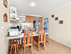 Una cocina compacta con armarios de madera, horno integrado y una zona de comedor con sillas y taburetes de madera.