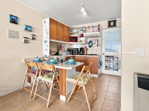 A compact kitchen with wooden cabinets, a central island with chairs, a refrigerator, and a window with a view. - Oceana Suites Bahía Pelicanos (Puchuncavi)
