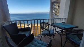 A balcony with a view of the ocean, a table, and two chairs.