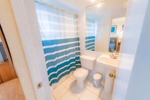 Een badkamer met een gestreept douchegordijn, een toilet, een wastafel en een spiegel.