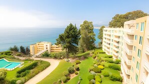 Een kusthotel met een zwembad, weelderige begroeiing en uitzicht op zee.