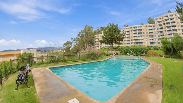 A rectangular swimming pool with a concrete edge, surrounded by a grassy area and a wooden fence.
