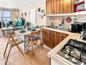 A kitchen with wooden cabinets, a gas stove, and a dining area with a table set for four. - Oceana Suites Bahía Pelicanos (Puchuncavi)